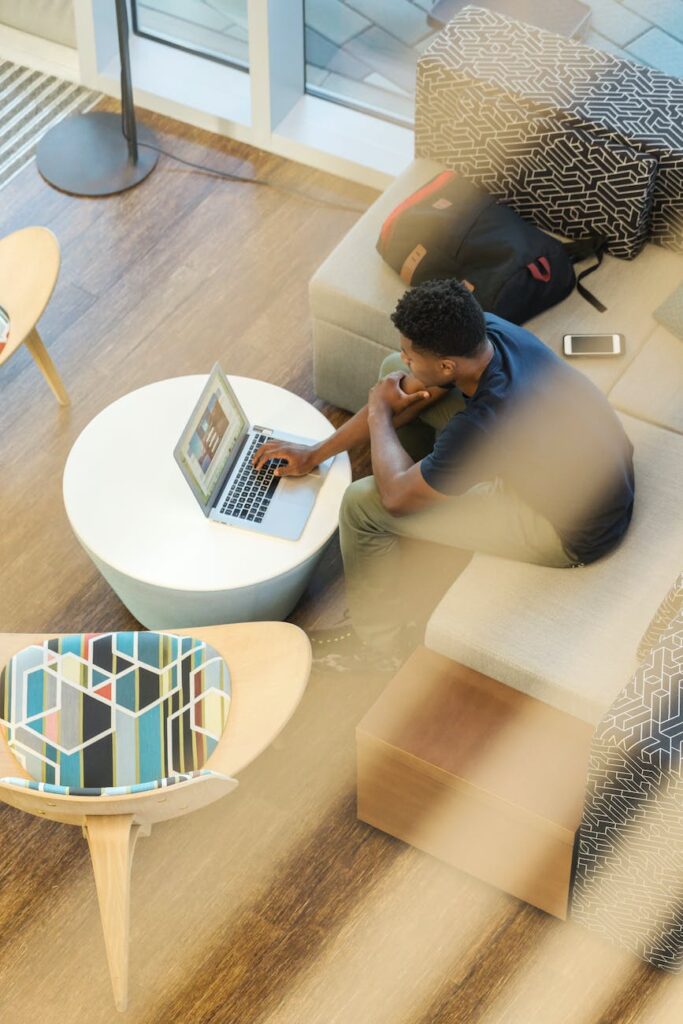 man using gray laptop while sitting on beige sofa